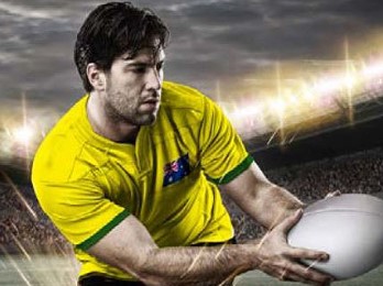A male rugby player in a yellow jersey is passing the ball. It's night time and he's playing in a large stadium