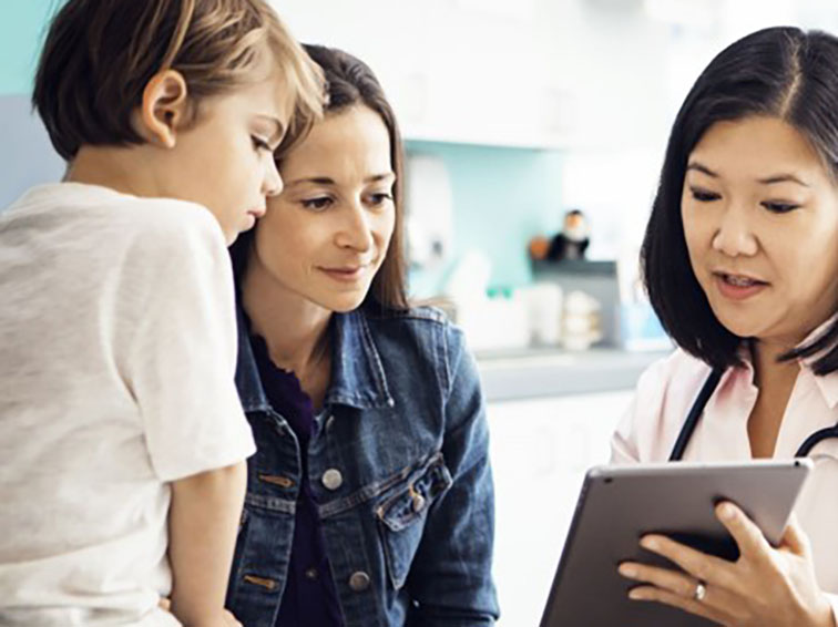 A researcher is pointing to a tablet which she is showing to a mother and her small child