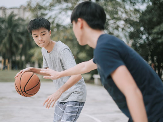 Two teenage boys are playing basketball on an outdoor court