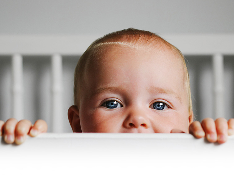 A baby looking over the railing of their cot